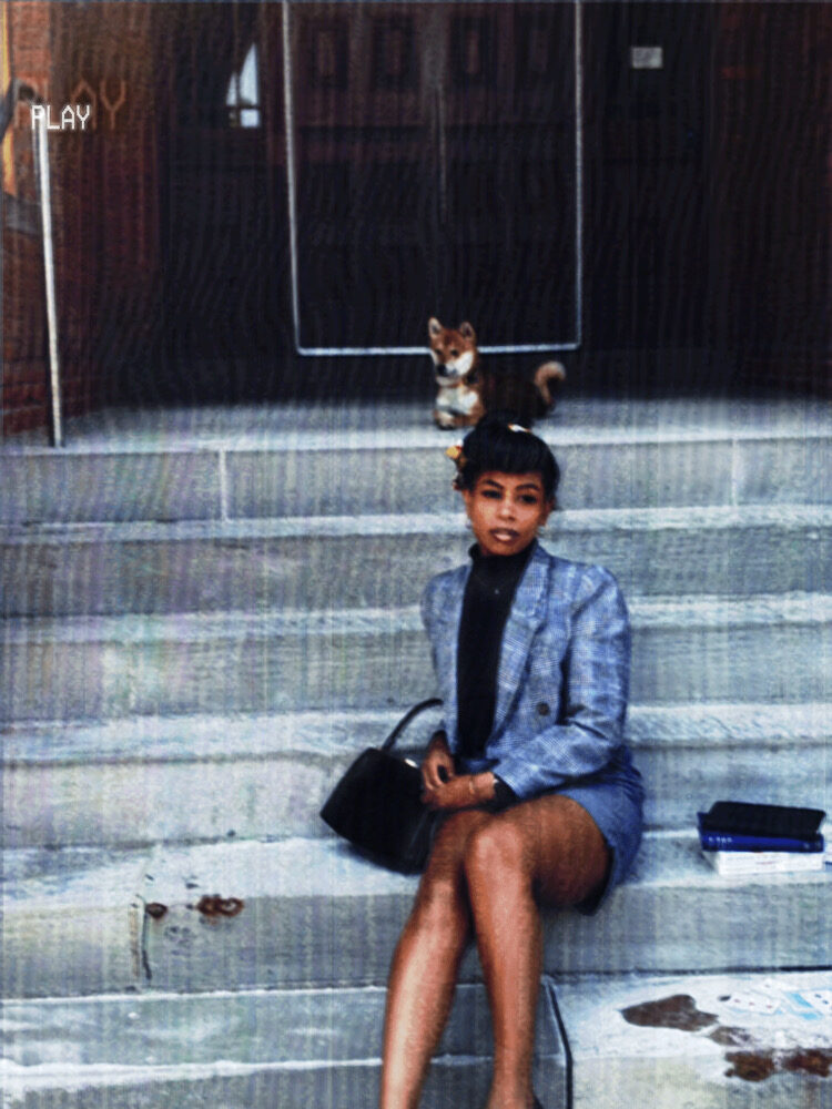 Tash Williamson in a heavily grained, vintage VHS-style photograph with a glowing "PLAY" icon in the corner, seated on outdoor stone steps holding a small black handbag in her lap, wearing a light blue plaid blazer over a black turtleneck and matching mini skirt; a small corgi sits on the steps behind her, a stack of books resting beside her on the stairs.