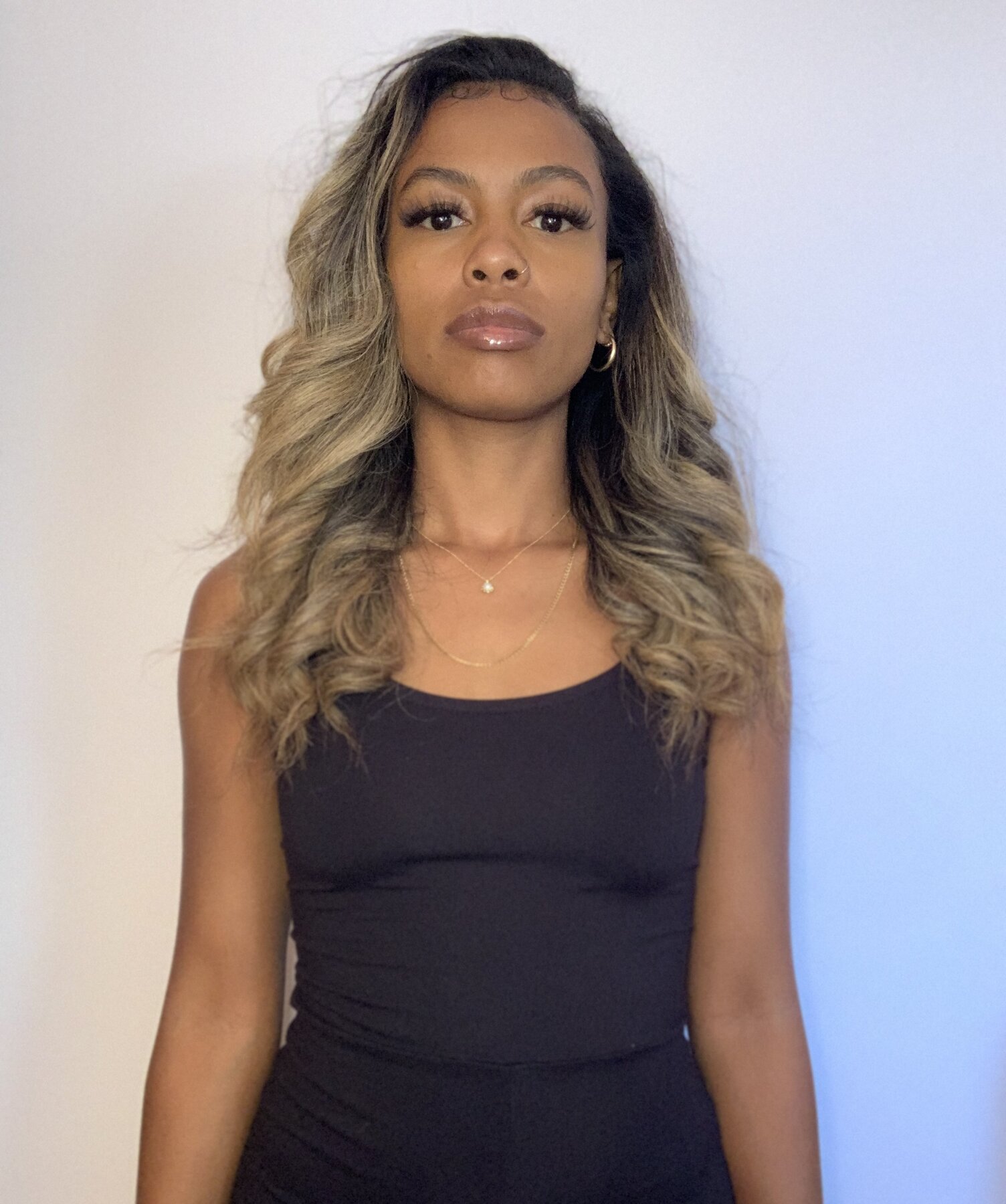 Tash Williamson in a front-facing waist-up portrait against a plain gray backdrop, wearing a black tank top, hair falling loosely on both sides framing the face, steady closed-mouth gaze.