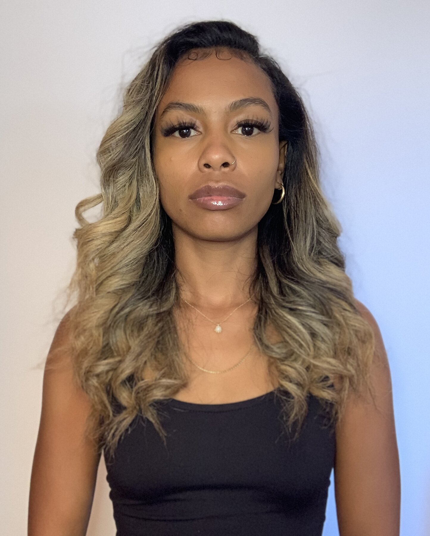 Tash Williamson in a closer front-facing portrait against a plain gray backdrop, wearing a black tank top with lips slightly parted, hair loose in soft waves.